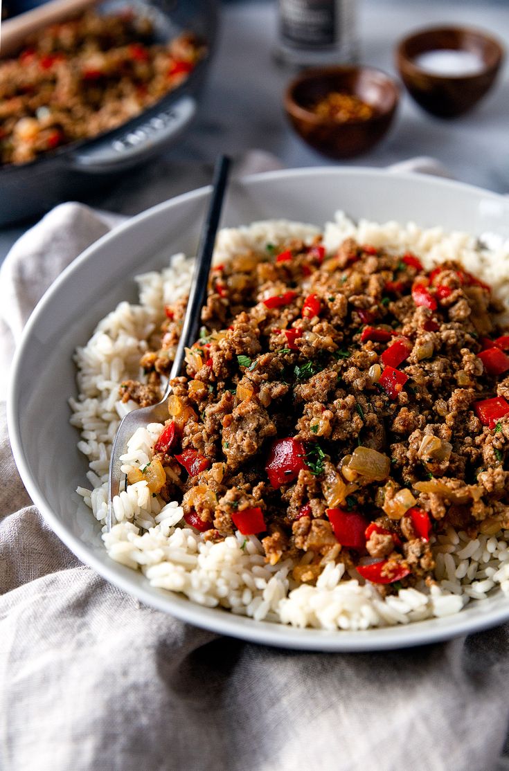 a white plate topped with rice covered in ground beef and red bell peppers on top