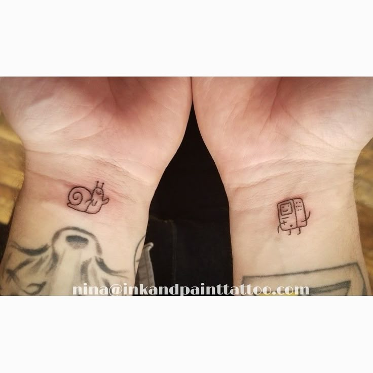 two people with matching tattoos on their wrists, one has an elephant and the other has a robot