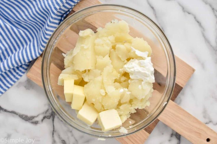 a glass bowl filled with cheese on top of a wooden cutting board next to a blue and white towel