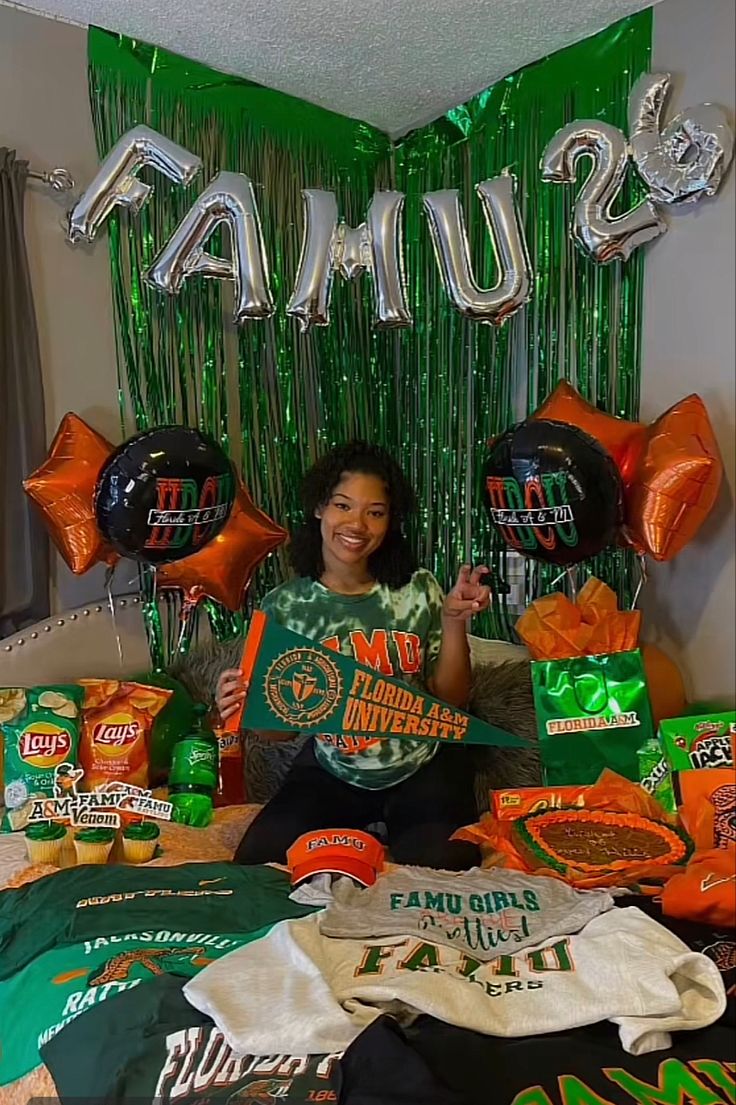 a woman sitting on top of a bed surrounded by green and orange balloons, t - shirts, and other items