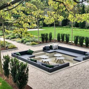 an outdoor seating area in the middle of a garden with trees and bushes around it