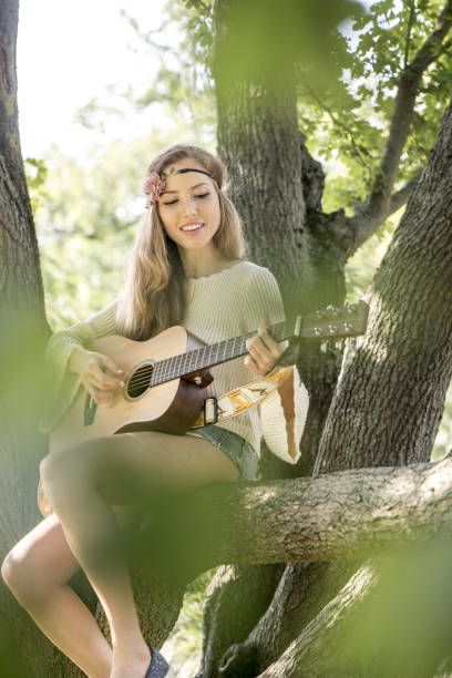 a woman sitting in a tree playing an acoustic guitar