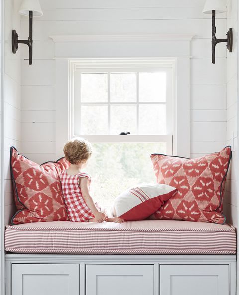 a woman sitting on top of a window sill with red and white pillows in front of her