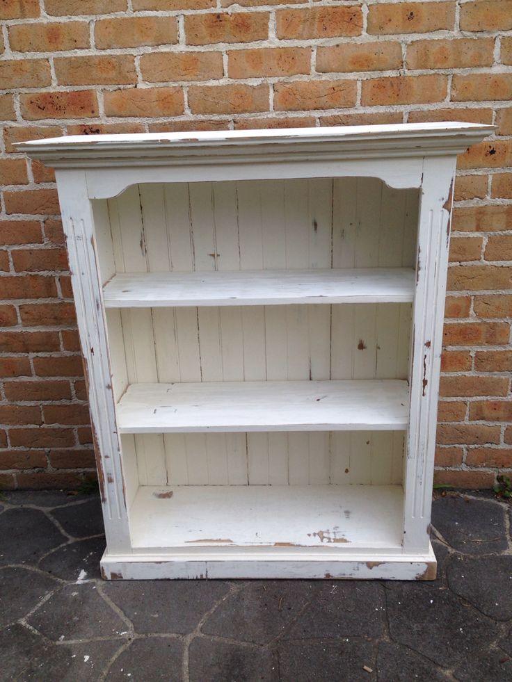 an old white painted bookcase against a brick wall