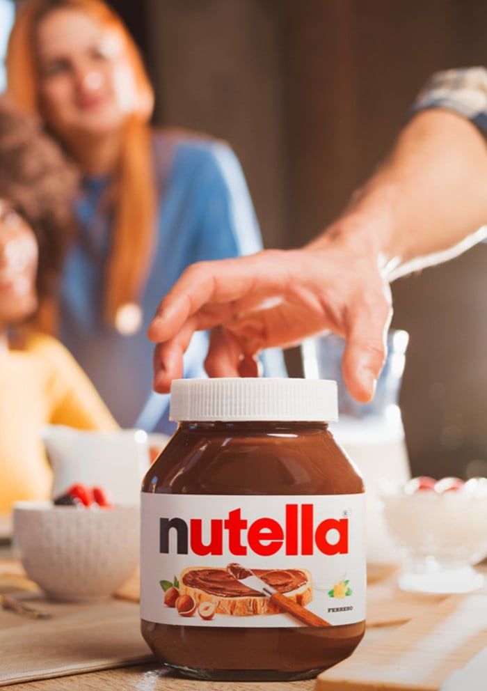 a nutella jar sitting on top of a wooden table next to two women and one man