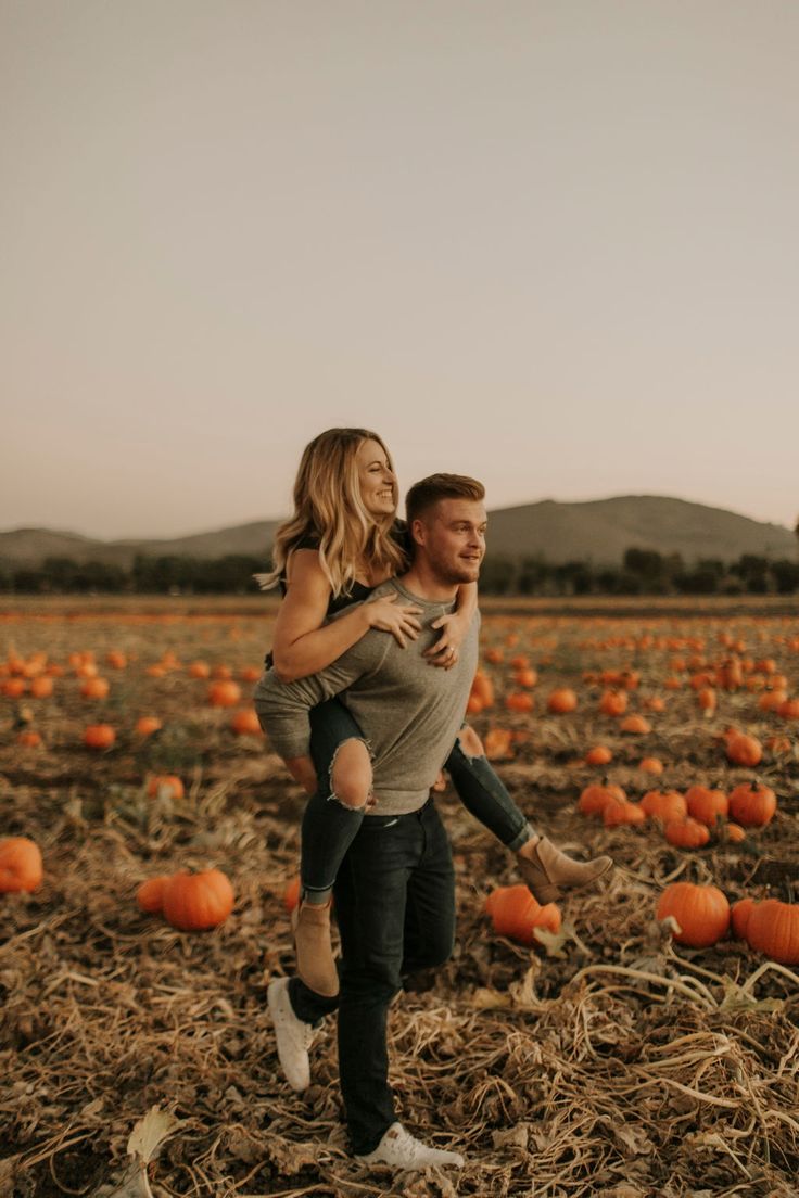 a man carrying a woman in a field full of pumpkins