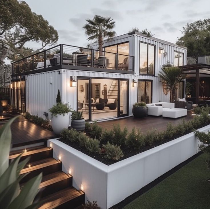 a modern house is lit up at night with lights on the porch and stairs leading to the upper level