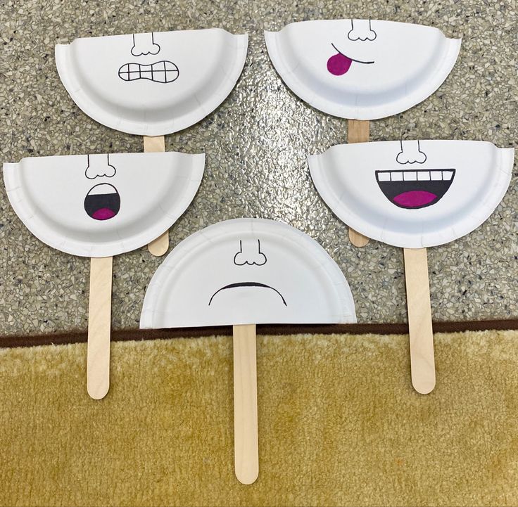 four paper plates with faces drawn on them sitting on a carpeted floor next to a rug