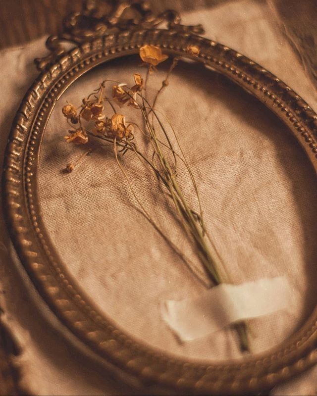 dried flowers are placed in an antique frame on a tablecloth covered with linens