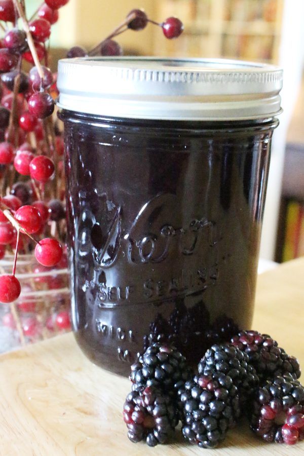 a jar filled with blackberries sitting on top of a table next to some berries