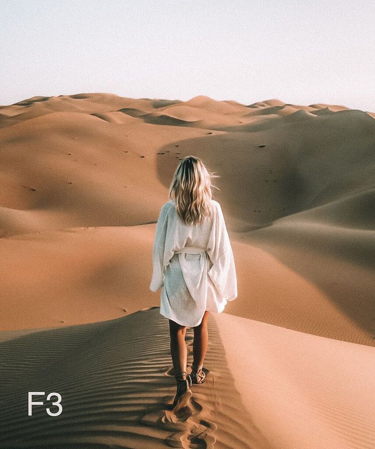 a woman walking in the desert with sand dunes