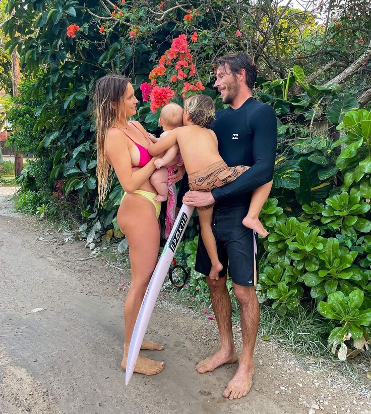 a man holding a surfboard while standing next to two women in bikinis and wetsuits