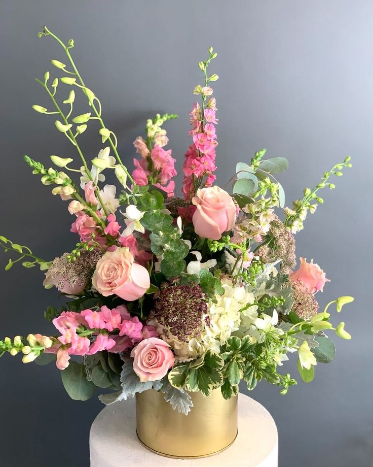 a gold vase filled with pink and white flowers on top of a cake covered in greenery