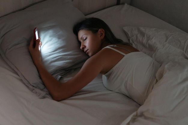 a woman laying in bed with her head on the pillow and holding a cell phone