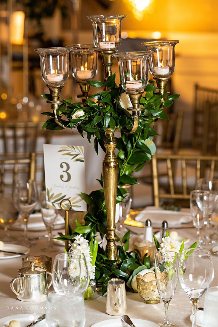 a tall gold candelabra with candles and flowers on it at a wedding reception