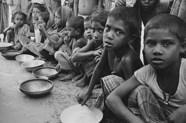 black and white photograph of children sitting at a table with plates in front of them