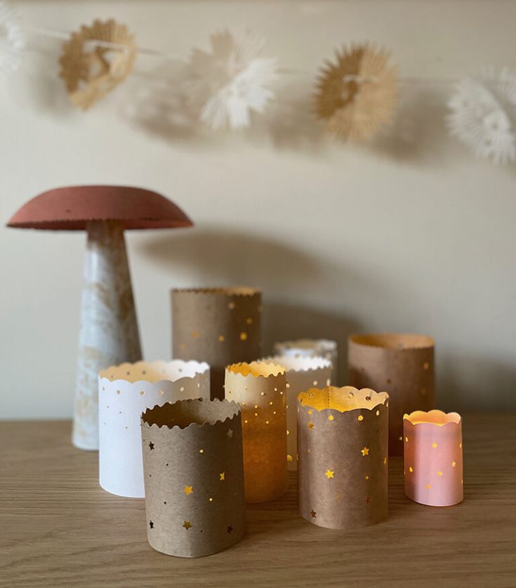 small candles are lined up on a table next to a mushroom shaped candle holder and paper lanterns