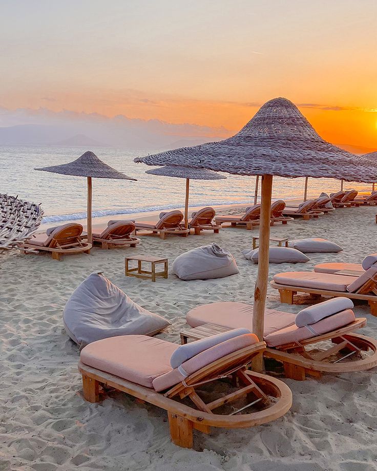 lounge chairs and umbrellas on the beach at sunset