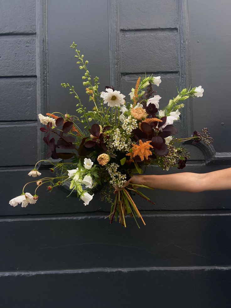 a person holding a bouquet of flowers in front of a black door with white and brown flowers