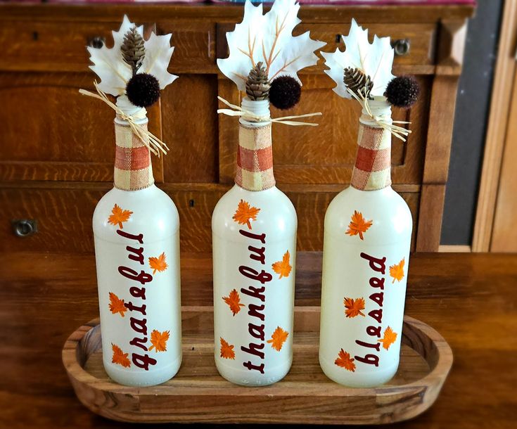 three wine bottles decorated with fall leaves and the words happy birthday are on a tray