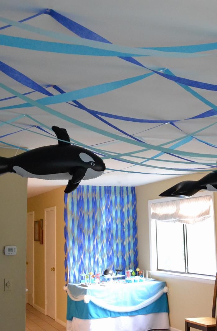 two fake orca whales are suspended from the ceiling in this bedroom decorated with blue streamers