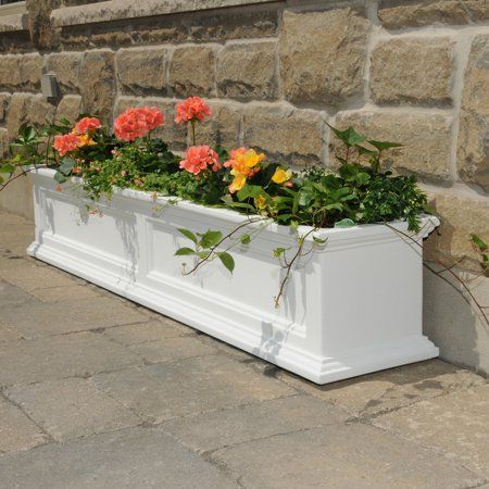 a white planter filled with lots of flowers next to a stone wall