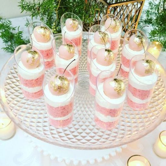 there are many small desserts on the glass platter with candles around it and greenery in the background