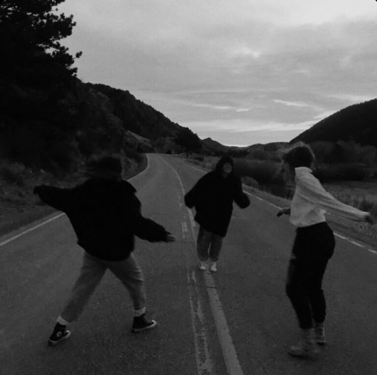 three people are skateboarding down the road in black and white, with mountains in the background