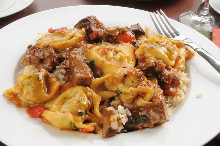 a white plate topped with pasta and meat covered in sauce on top of a wooden table