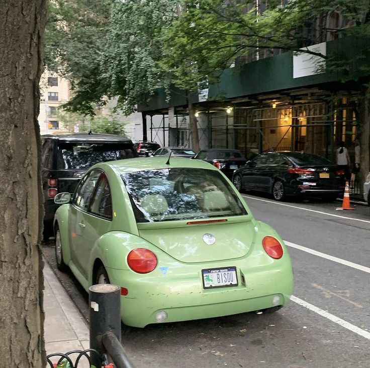 a small green car parked on the side of a street next to a tree and parking meter