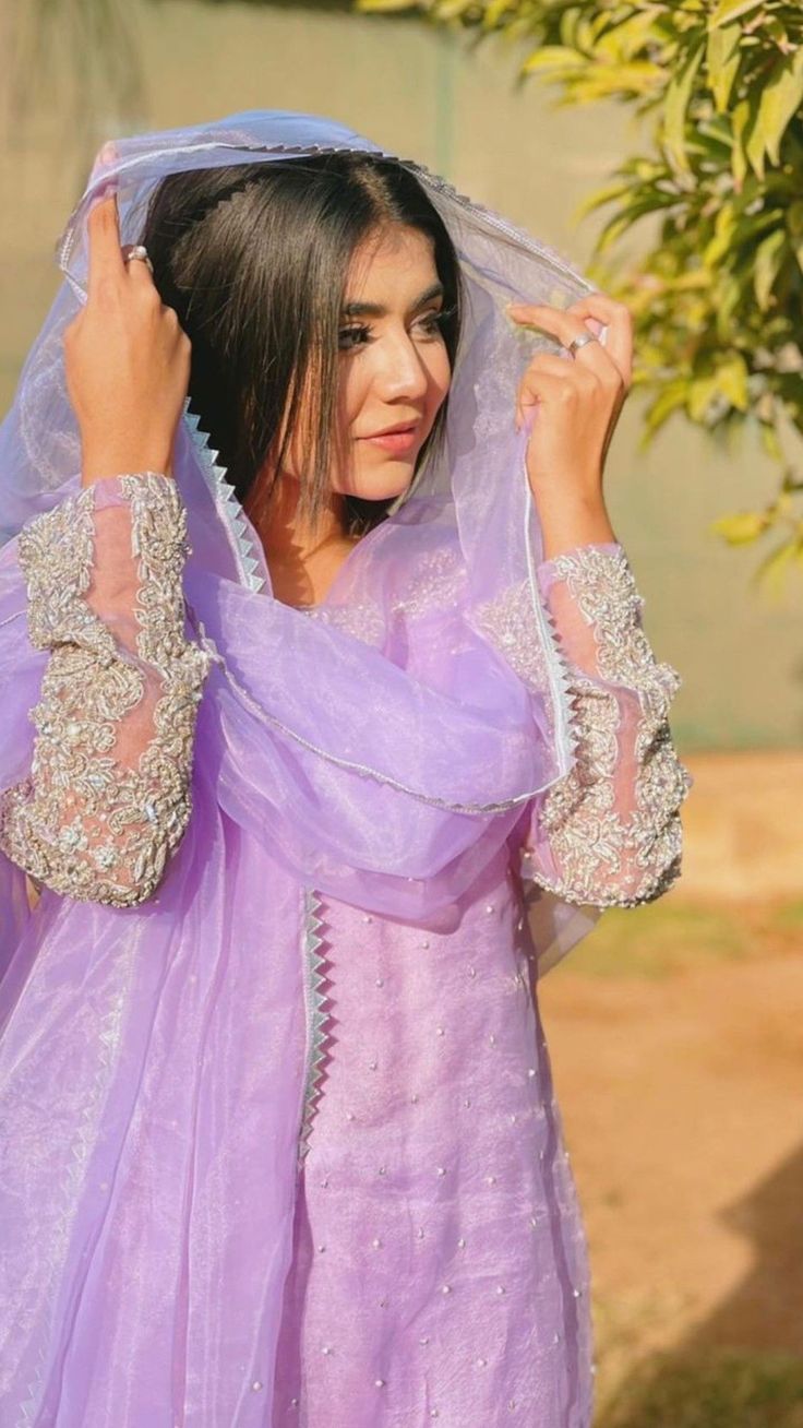 a woman in a purple dress is holding her veil over her head and looking off to the side