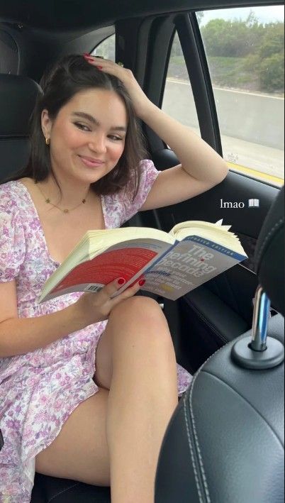 a young woman sitting in the back seat of a car reading a book and smiling