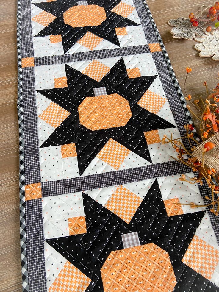 an orange and black quilted table runner on top of a wooden floor next to flowers