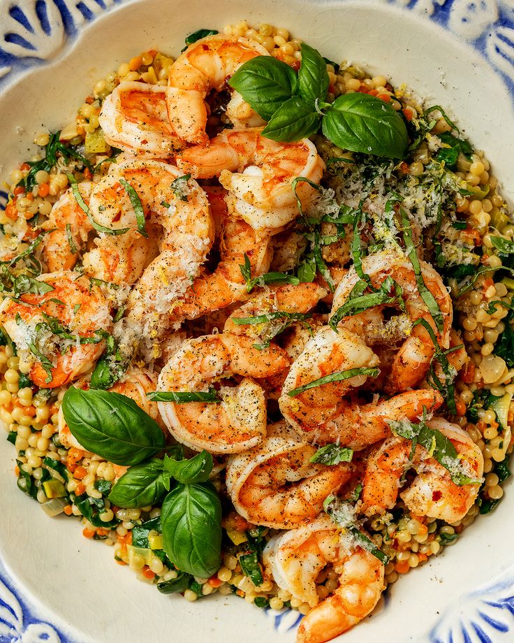 a white bowl filled with shrimp, corn and spinach on top of a blue and white table cloth