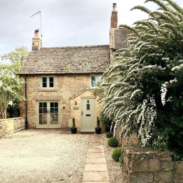 an old stone house with a green door and white flowers in the front yard on a cloudy day