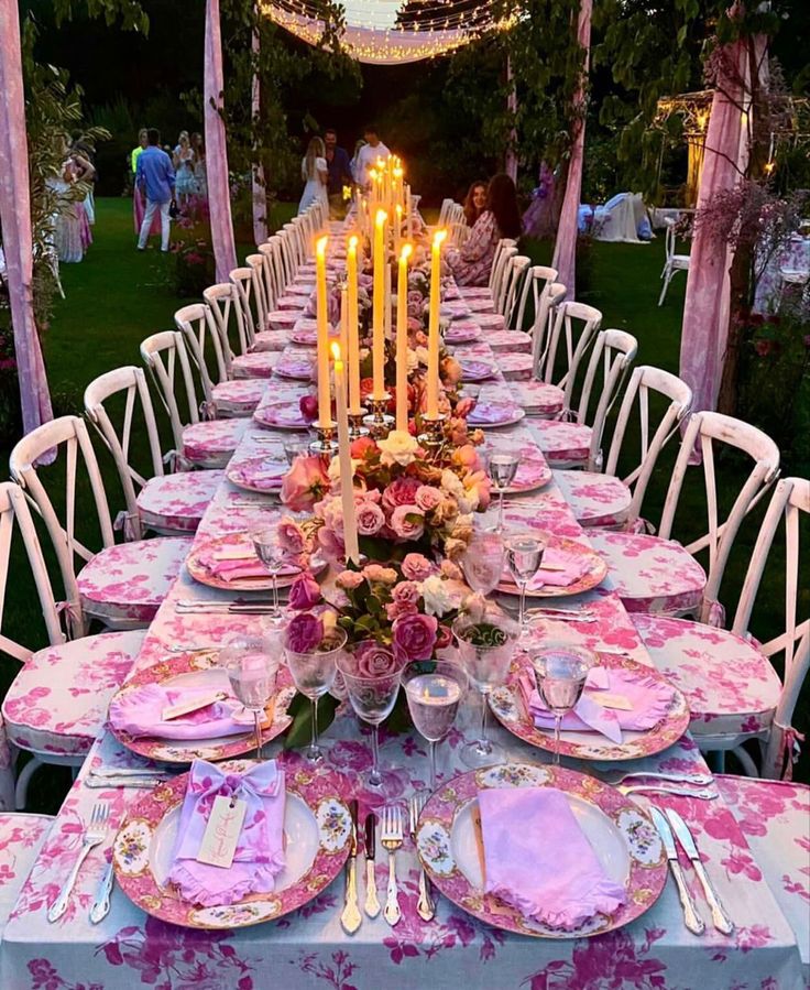 a long table is set with pink and white plates, silverware, and candles