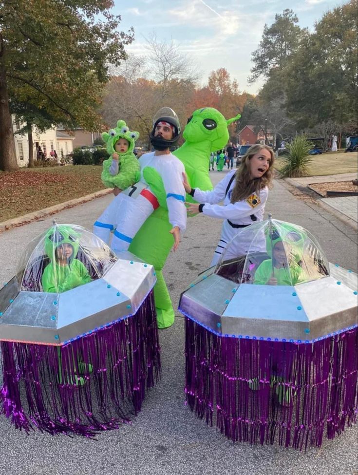 three people in costume standing next to two large objects on the street with purple fringes