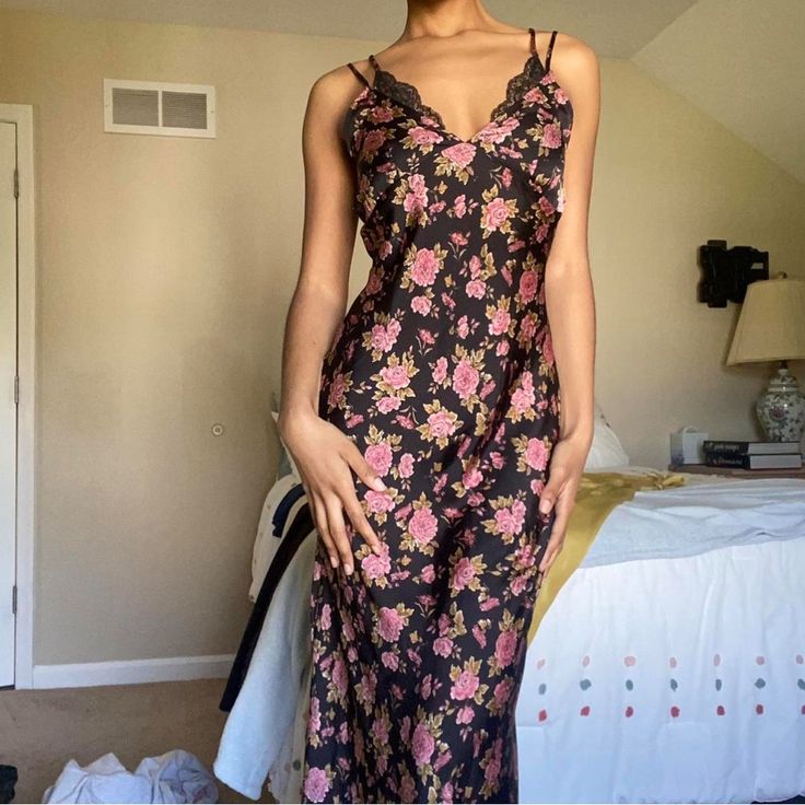 a woman standing in front of a bed wearing a black and pink floral print dress