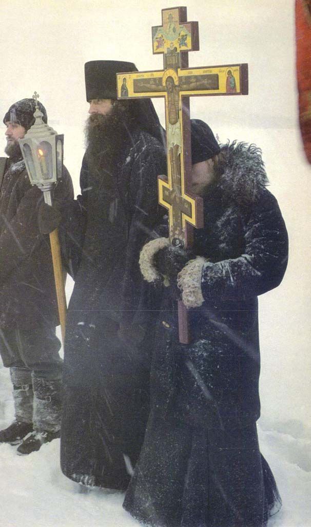 two people standing in the snow with a crucifix on their head and one holding a lantern