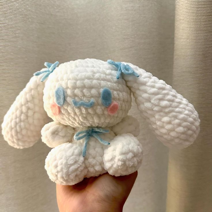 a hand holding a small white crocheted stuffed animal