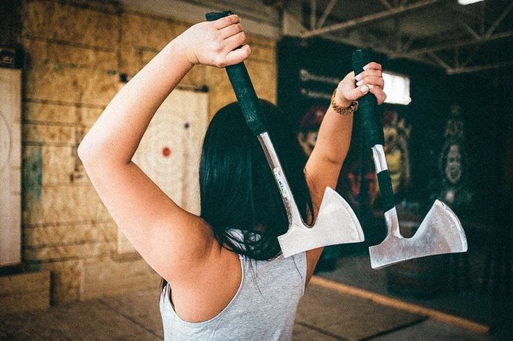 a woman holding two large hammers up to her head with one hand and the other arm in the air