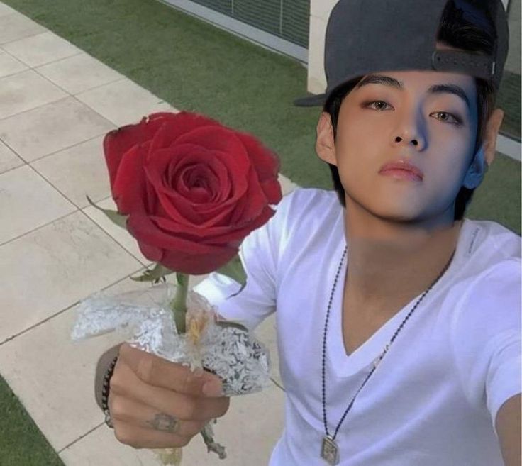 a young man holding a red rose in his right hand and wearing a baseball cap