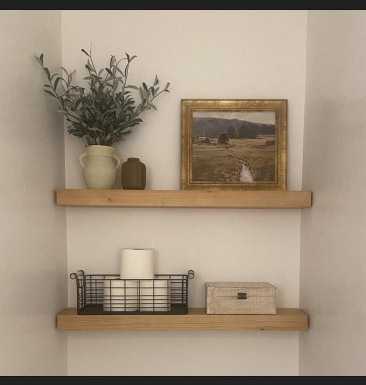 two wooden shelves in a bathroom next to a toilet and a painting on the wall