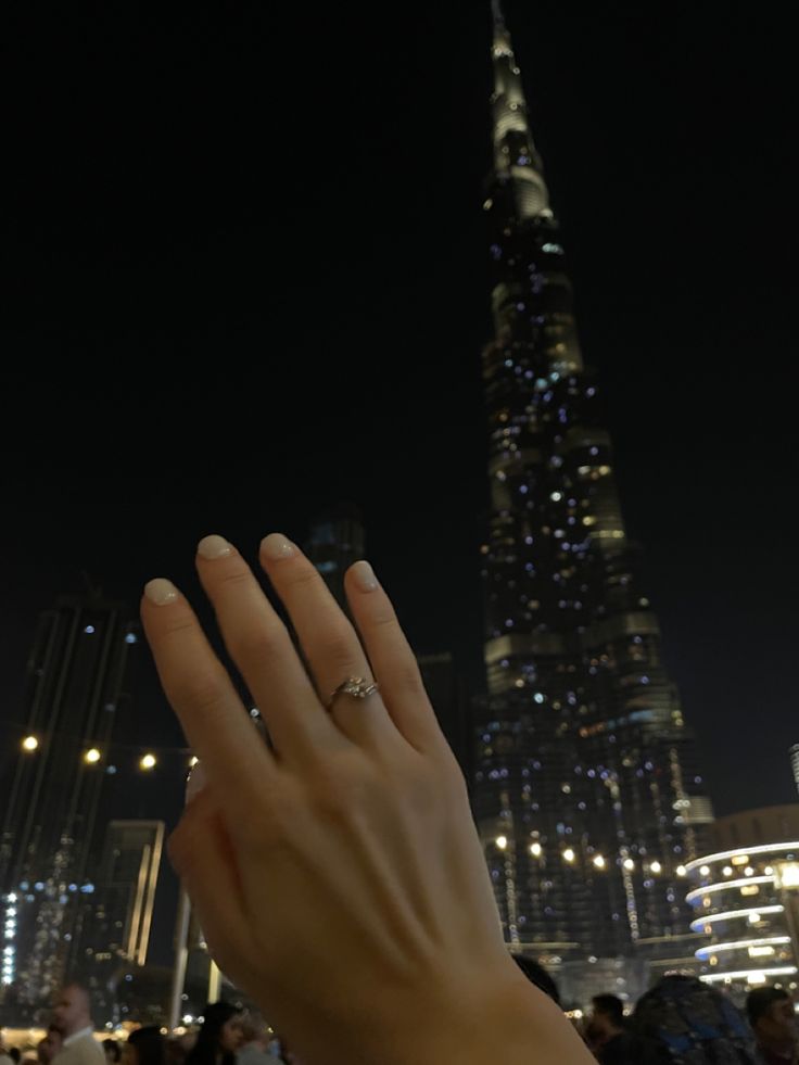 a person holding their hand up in front of a very tall building with lights on it