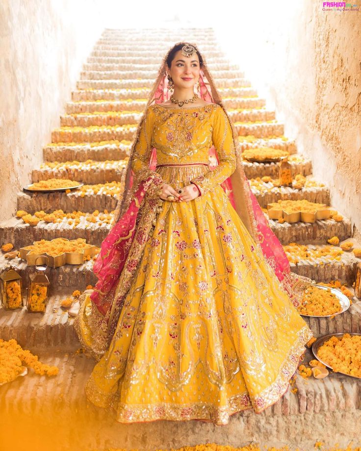 a woman in a yellow wedding dress standing on some steps with flowers all around her