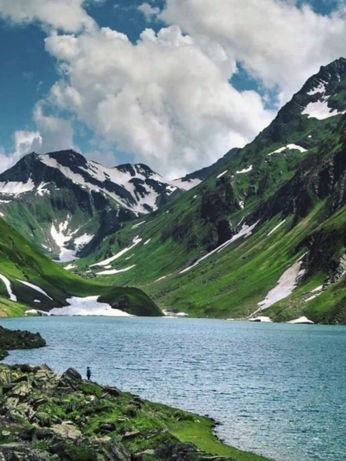 a man standing on the side of a mountain next to a lake