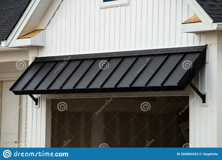 an awning on the side of a white house with black shingles and windows