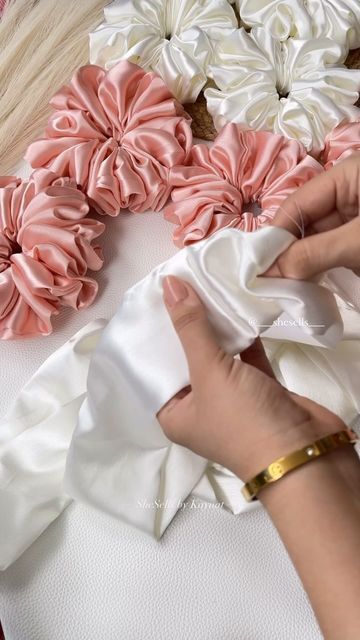 a woman is working on some fabric with flowers in the background and another person's hand