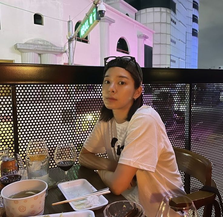 a woman sitting at a table with food and drinks on it in front of a building