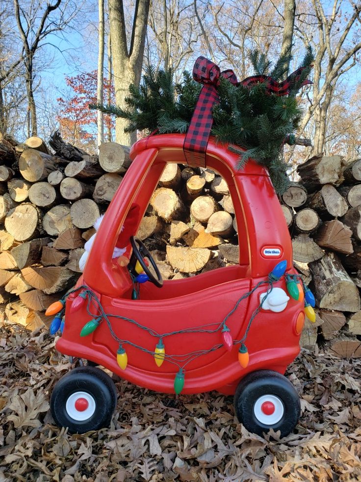 a red toy car with christmas lights on it's roof is parked in front of a pile of wood